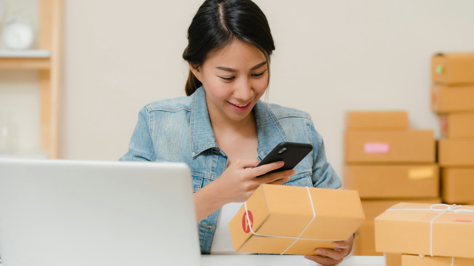 Empreendedora conferindo um pedido no celular ao lado de caixas de envio